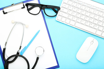 Stethoscope with clipboard, eyeglasses and keypad on blue background