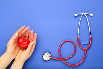 Stethoscope and female hands with red heart on blue background