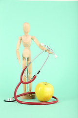 Stethoscope with apple and wooden figure on mint background