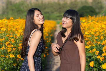 Asian cute two sister woman joyful, smiling with yellow cosmos background.