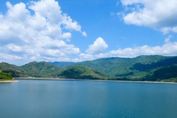 The road beside the reservoir with mountains in the background, blue sky and white clouds