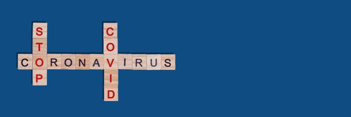 Banner. Text crossword puzzle of wooden red and black letters stop coronavirus covid on a blue classic background. Concept of ending quarantine, protection from spread of viral infection. Copy space.