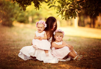 Young beautiful mother with two little daughters sitting under th tree