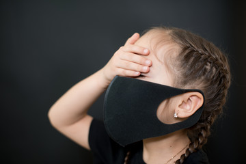 Young girl in protective sterile medical mask on her face, closes his eyes with his hand on a black background. Coronavirus Covid-19 pandemia concept.