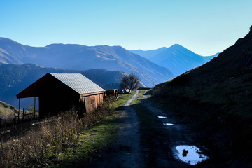 A pathway crosses a house on the left and an ancient tower on the right in Omala - Tusheti