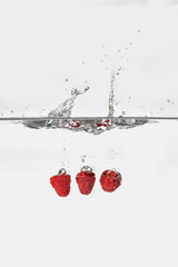 ripe red raspberries splashing in transparent water