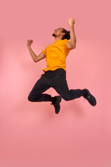 Fototapeta na wymiar Full length shot of a cheerful funny black man in sneakers, crazy flying carefree jumping with raised arms, celebrating victory, having fun, rest, relax and leisure, isolated on pink background