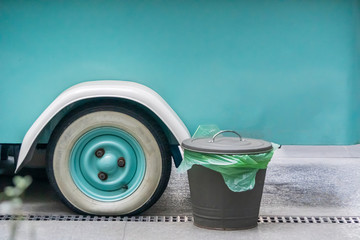 A metal urn with a lid and a green bag for mixed garbage and cigarette butts near the wheel of a car or food truck on a city street. separate waste collection. Copyspace