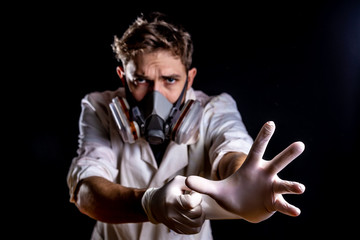 Caucasian male with dark sunglasses wearing half face respirator or gas mask reaching hand towards camera, dark background with dramatic lighting effects in dusty enviroment. Virus fear concept.