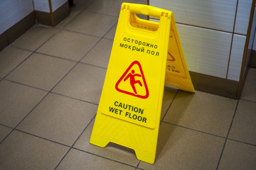 Warning sign with Russian text caution wet floor. Sign in the corridor of the office or entertainment center. Cleaning ceramic tiles in the toilet. Copy space.