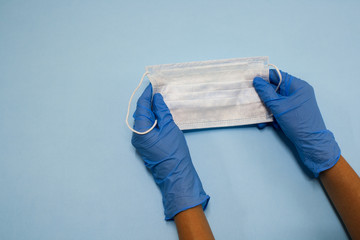 Blue gloved hands holding medical surgical mask on blue background
