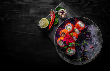 sushi roll with salmon, avocado, cream cheese in plate on black wooden table background