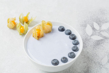 Healthy Breakfast smoothie bowl with coconut yogurt, blue matcha tea, blueberries and physalis.