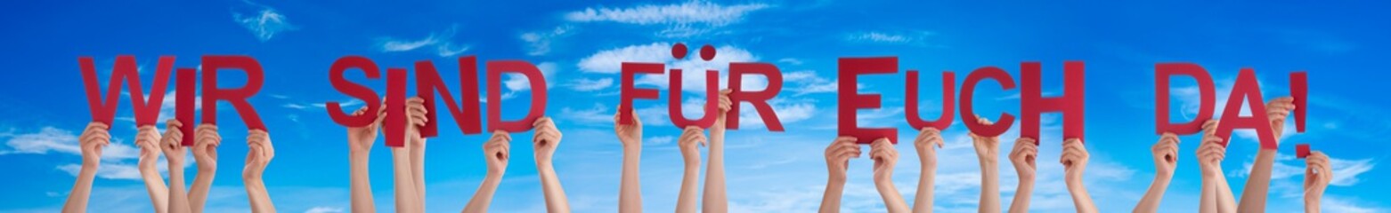 People Hands Holding Colorful German Word Wir Sind Fuer Euch Da Means We Are Here For You. Blue Sky As Background