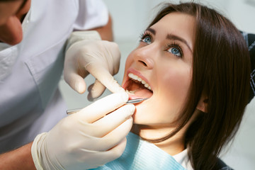 Dentist examining a patient's teeth in modern dentistry office. Closeup cropped picture with copyspace. Doctor in disposable medical facial mask.