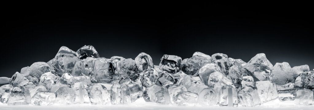 Heap of translucent crushed ice cubes on black background. Wide format.