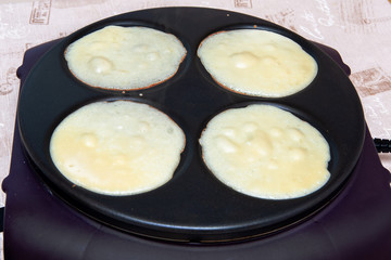 Close-up of the dough for four pancakes is cooked in an electric pan, top view