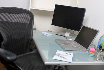 Empty view of deserted office cubicle featuring a desk chair, laptop computer and blank secondary screen for creative work