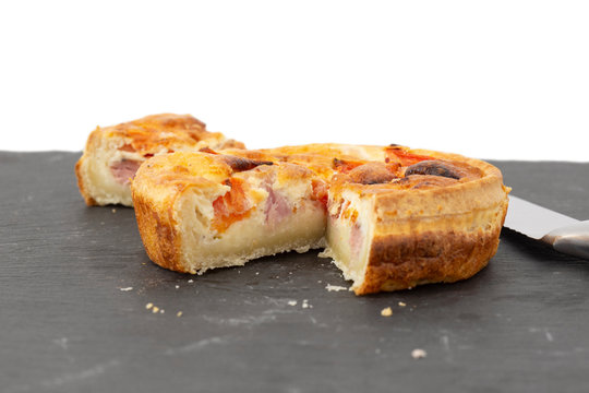 Ham and tomato quiche sliced with a knife.  On a slate chopping board with a white background