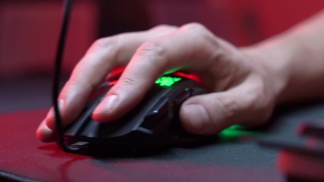 Gaming Device Mouse. A gamer is playing in a computer club. In the frame, the hand of a gamer and a gaming mouse. Red and violet colors. ESports competitions.

