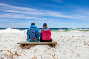 Paar sitzt verträumt am Strand und schaut auf die Wellen am Meer