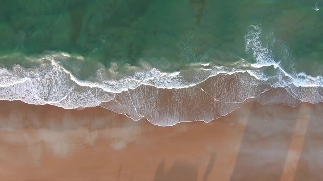 Pretty blue ocean waves crashing on shore at sunset.