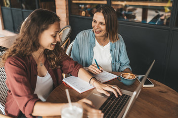 Two women discussing business projects in a cafe while having coffee.
