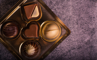 Five delicious chocolate bonbons in a golden box on gray background. Horizontal format. Aerial view.