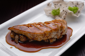 Chicken fillet with teriyaki sauce, on a white plate, against a dark background