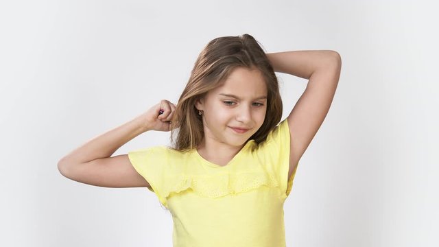 a little Girl combs her hair. Girl in yellow dress on white background Rosse his long hair and smiling.