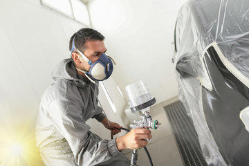 Car body worker paints a car in the paint booth with a spraying paint