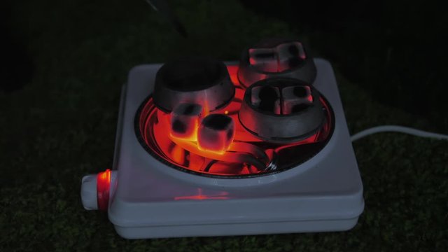 Close up of hot red coals for hookah. Smoldering coals being heated for shisha. Closeup man hand holding red-hot coal with tongs.