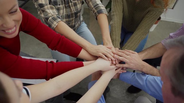 Tilt down top view shot of therapist and diverse patients putting hands together to support and encourage each other sitting in circle at group therapy session