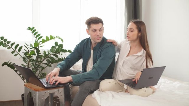 Stay home. Beautiful couple at home. Man work at home, he is in freelance during quarantine coronavirus, he use laptop.