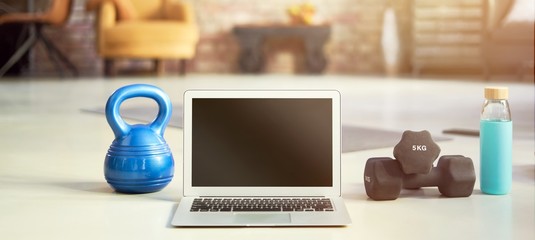Blank screen laptop and fitness equipments at home. Concepts about online workout program, fitness video, home workout.