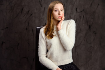 Studio portrait of a pretty caucasian blonde girl showing different emotions. A woman sits on a chair on a gray stylish background.