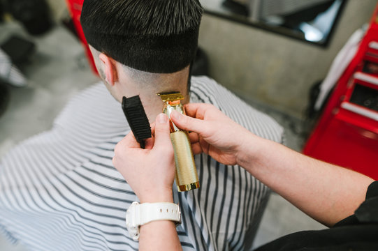 Professional male hairdresser cuts her client's hair with a gold trimmer and holds a close-up photo in her hands. Creating stylish male haircut in barbershop, concept. Copy space