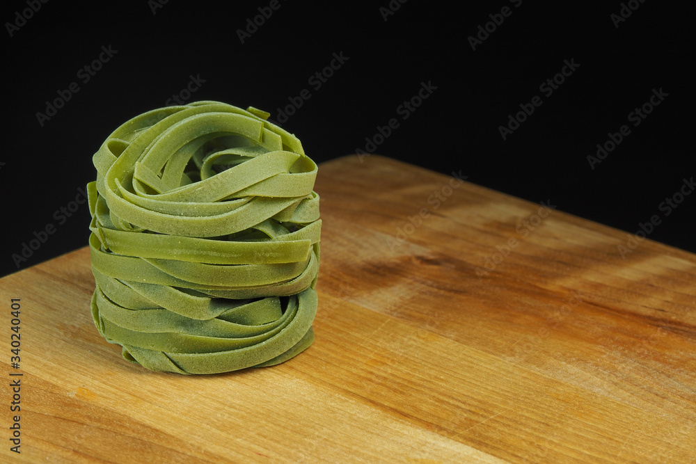 Wall mural green noodles with spinach twisted in the form of a nest on a black background