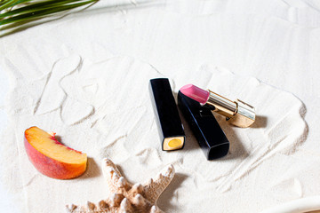 Wonderful beach. Lipstick, lip gloss, lip balm lie on the sand, surrounded by juicy fruits,...