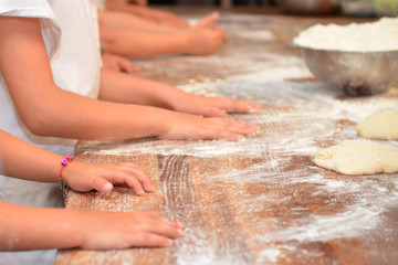 Little kids make dough products. Flour is scattered around. Hands close up.