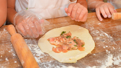 Little kids make dough products. Flour is scattered around. Hands close up.