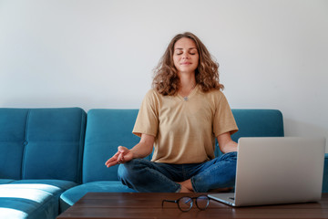Calm healthy young woman taking break  with eyes closed sit on blue sofa with laptop,  breathing...