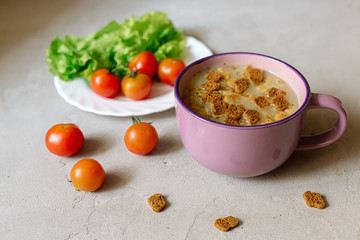 Soup with rye crackers, lettuce and fresh cherry tomatoes on a gray background
