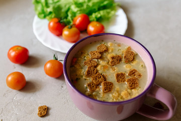 Soup with rye crackers, lettuce and fresh cherry tomatoes on a gray background
