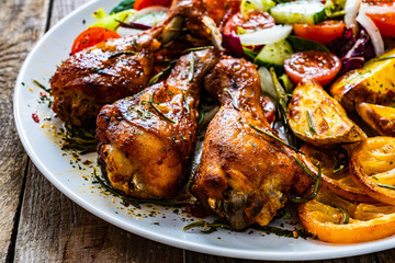 Barbecue chicken drumsticks with vegetables on wooden table