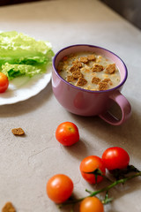 Soup with rye crackers, lettuce and fresh cherry tomatoes on a gray background
