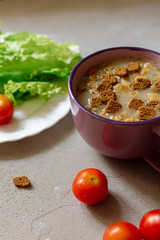 Soup with rye crackers, lettuce and fresh cherry tomatoes on a gray background
