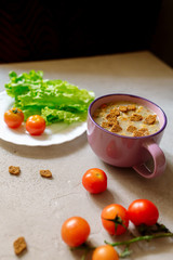 Soup with rye crackers, lettuce and fresh cherry tomatoes on a gray background

