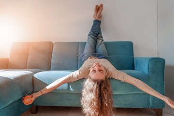 Portrait of  lovely  cheerful cheery curly girl having fun lying on blue sofa with head upside...