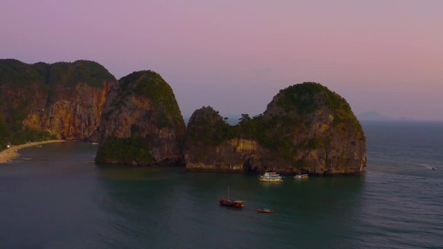 Drone shot of island beach in Thailand in the sunset, few boats there.